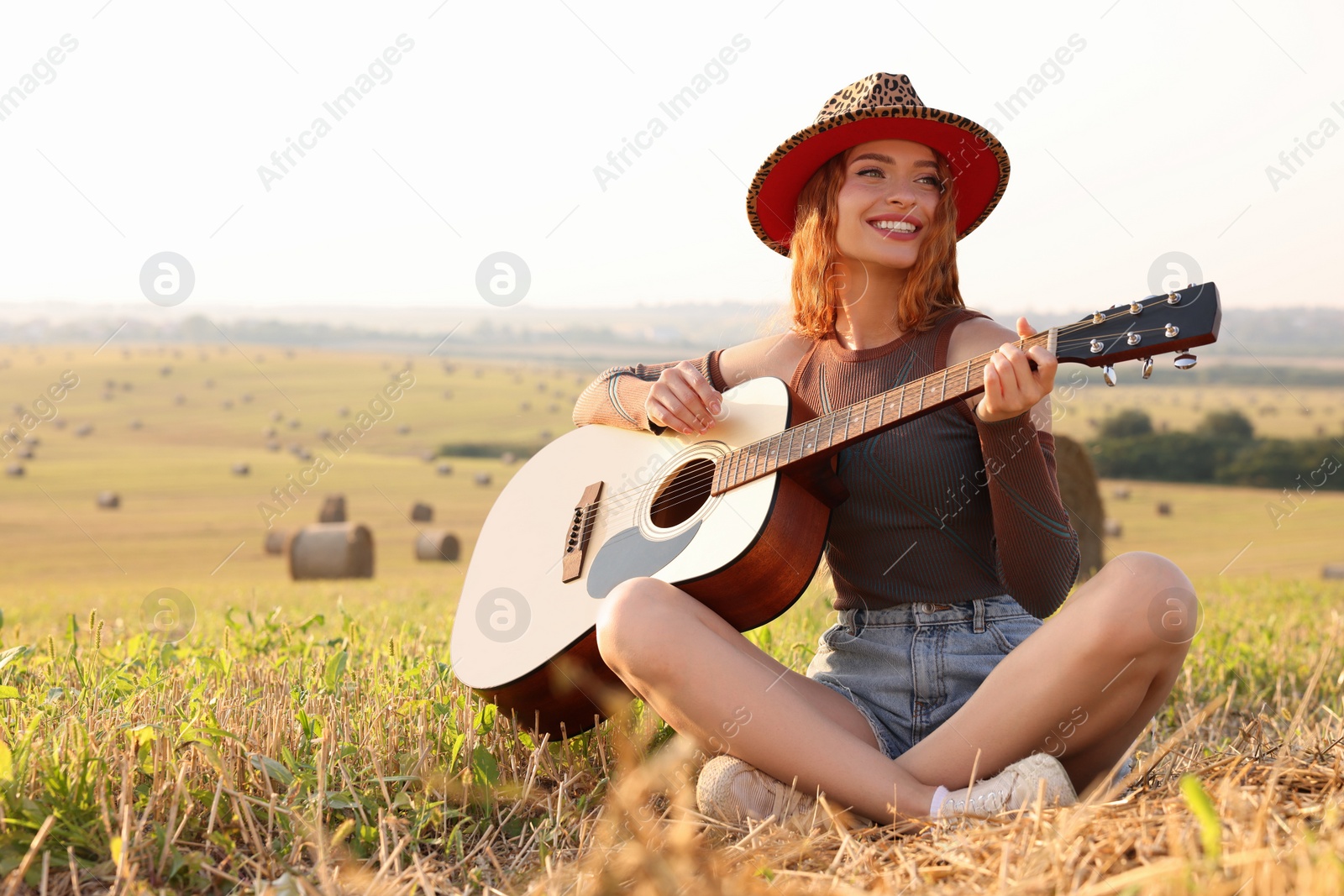 Photo of Beautiful happy hippie woman playing guitar in field, space for text