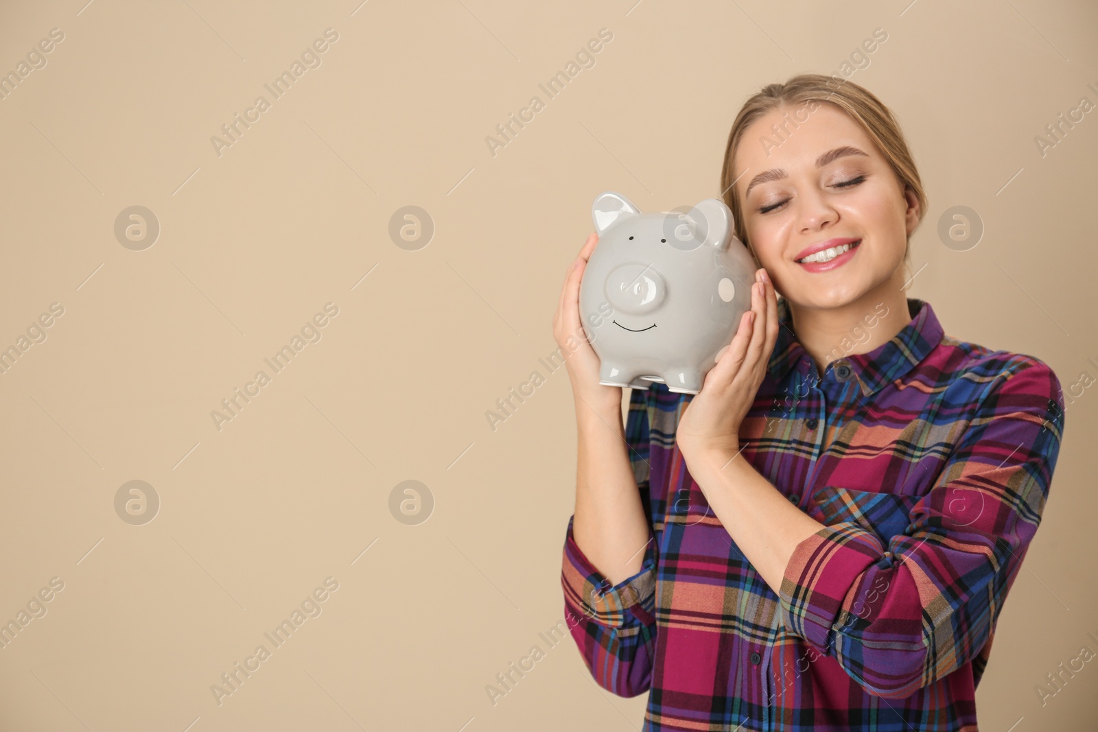 Photo of Happy young woman with piggy bank and space for text on color background. Money saving