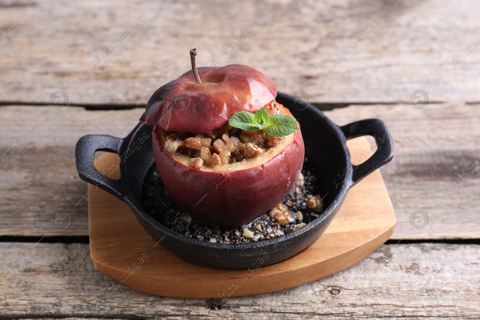 Photo of Tasty baked apple with nuts, honey and mint in baking dish on wooden table