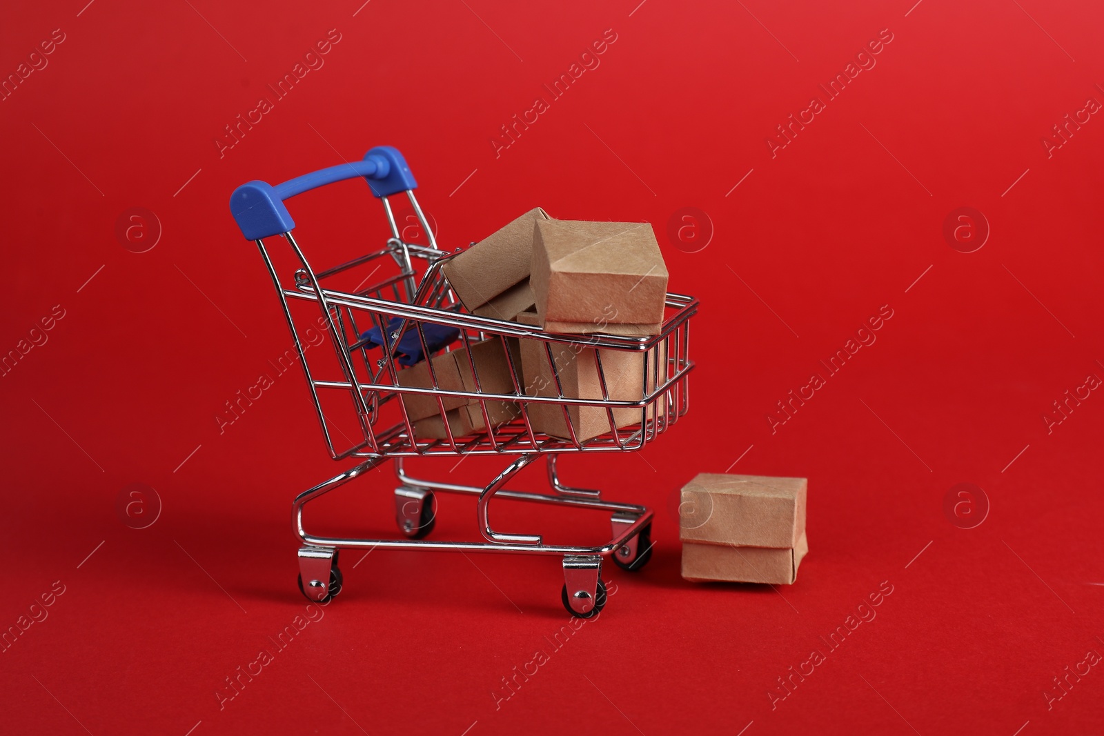 Photo of Small metal shopping cart with cardboard boxes on red background
