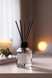 Photo of Reed diffuser on white table indoors. Cozy atmosphere