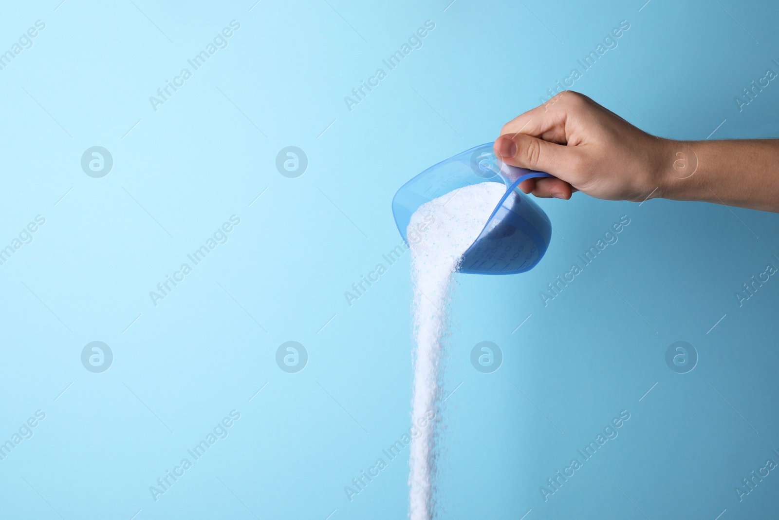 Photo of Woman pouring laundry detergent from measuring container against blue background, closeup. Space for text