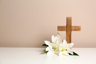 Photo of Composition with wooden cross and blossom lilies on table against color background, space for text