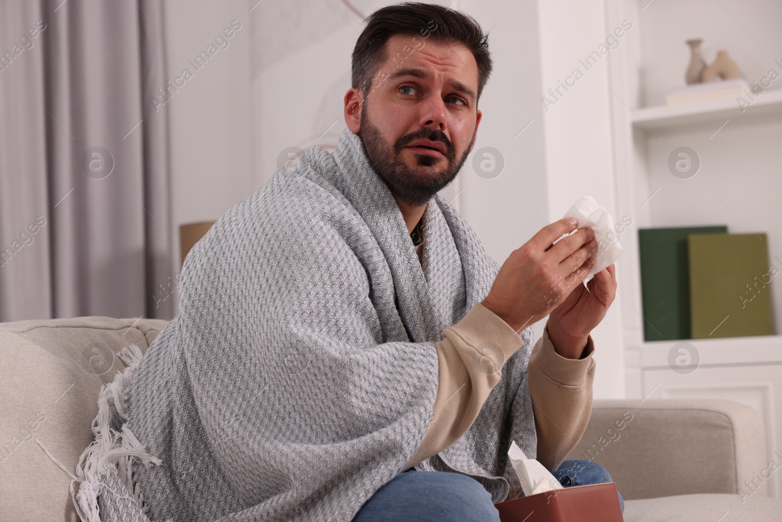 Photo of Sick man wrapped in blanket with tissues on sofa at home. Cold symptoms