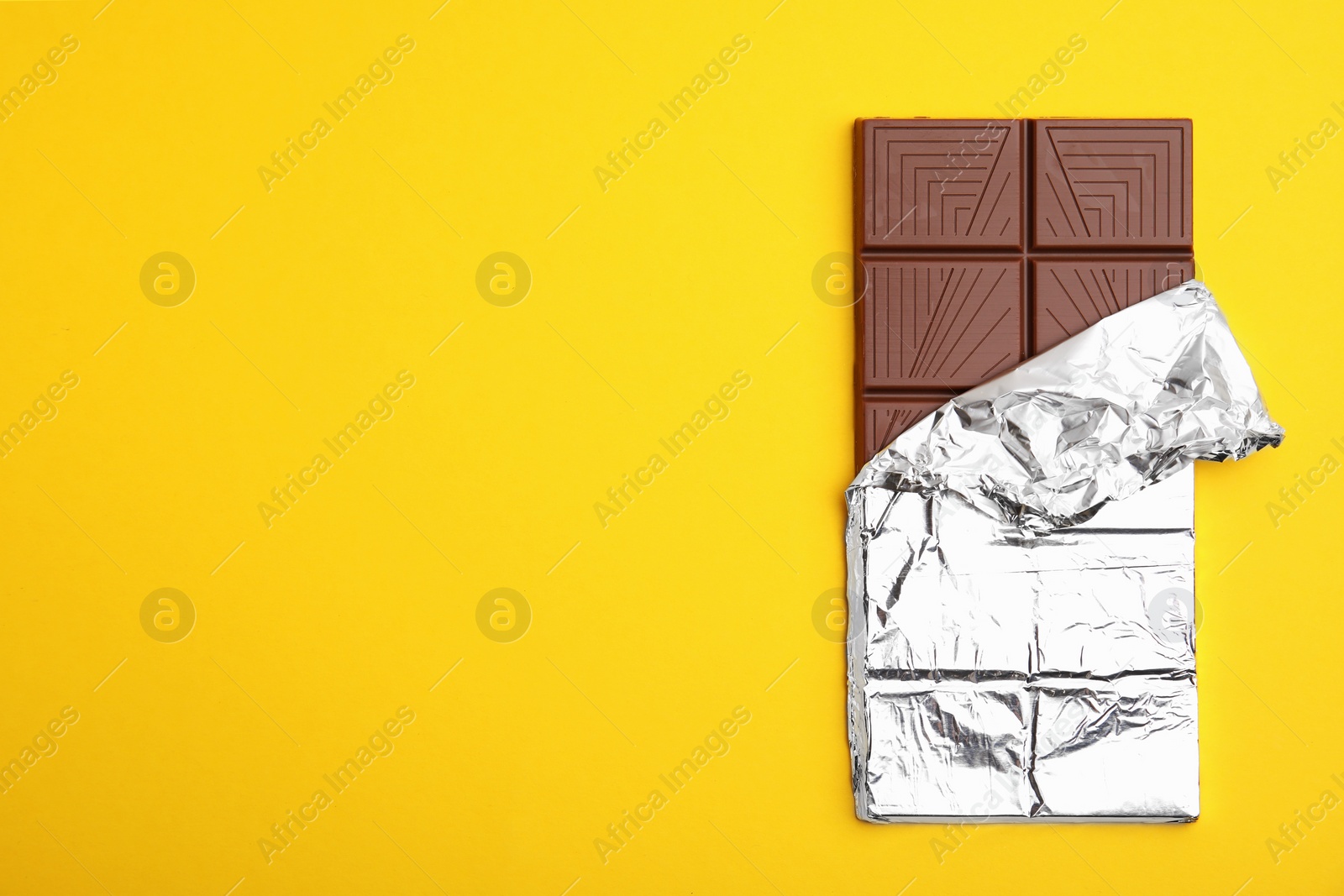 Photo of Tasty chocolate bar on yellow background, top view. Space for text