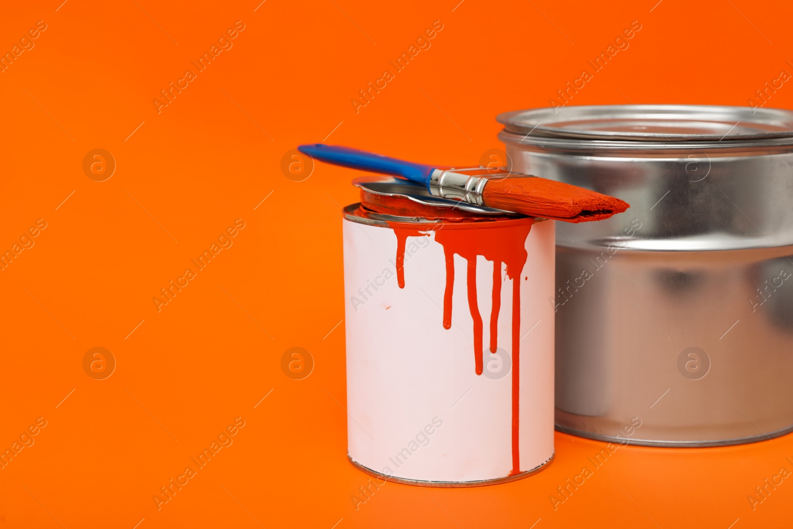 Photo of Cans of orange paint and brush on color background. Space for text