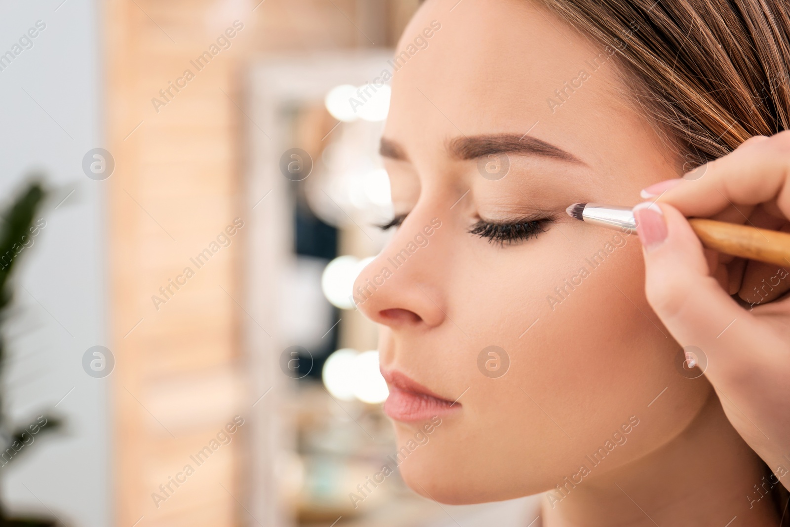 Photo of Professional visage artist applying makeup on woman's face in salon, closeup