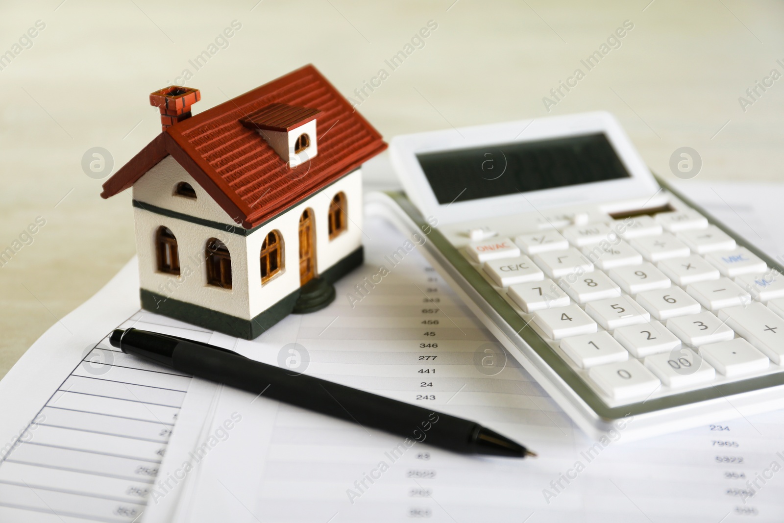 Photo of Calculator, house model, pen and documents on light table. Real estate agent's workplace