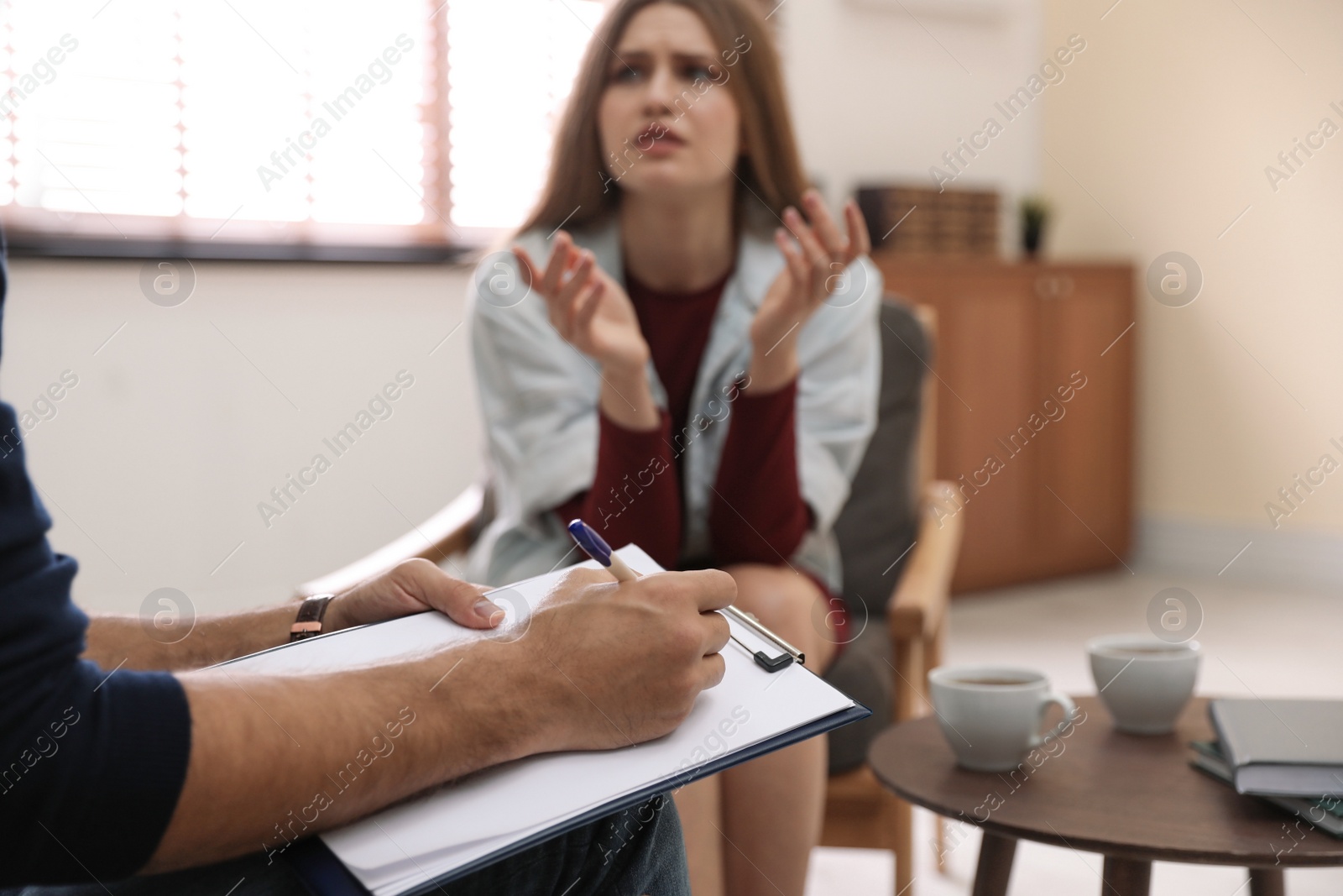 Photo of Professional psychotherapist and patient in office, focus on hands with clipboard