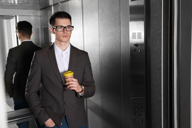 Young businessman with cup of hot drink in elevator