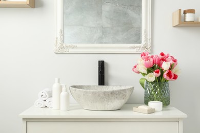 Photo of Vase with beautiful pink tulips and toiletries near sink in bathroom