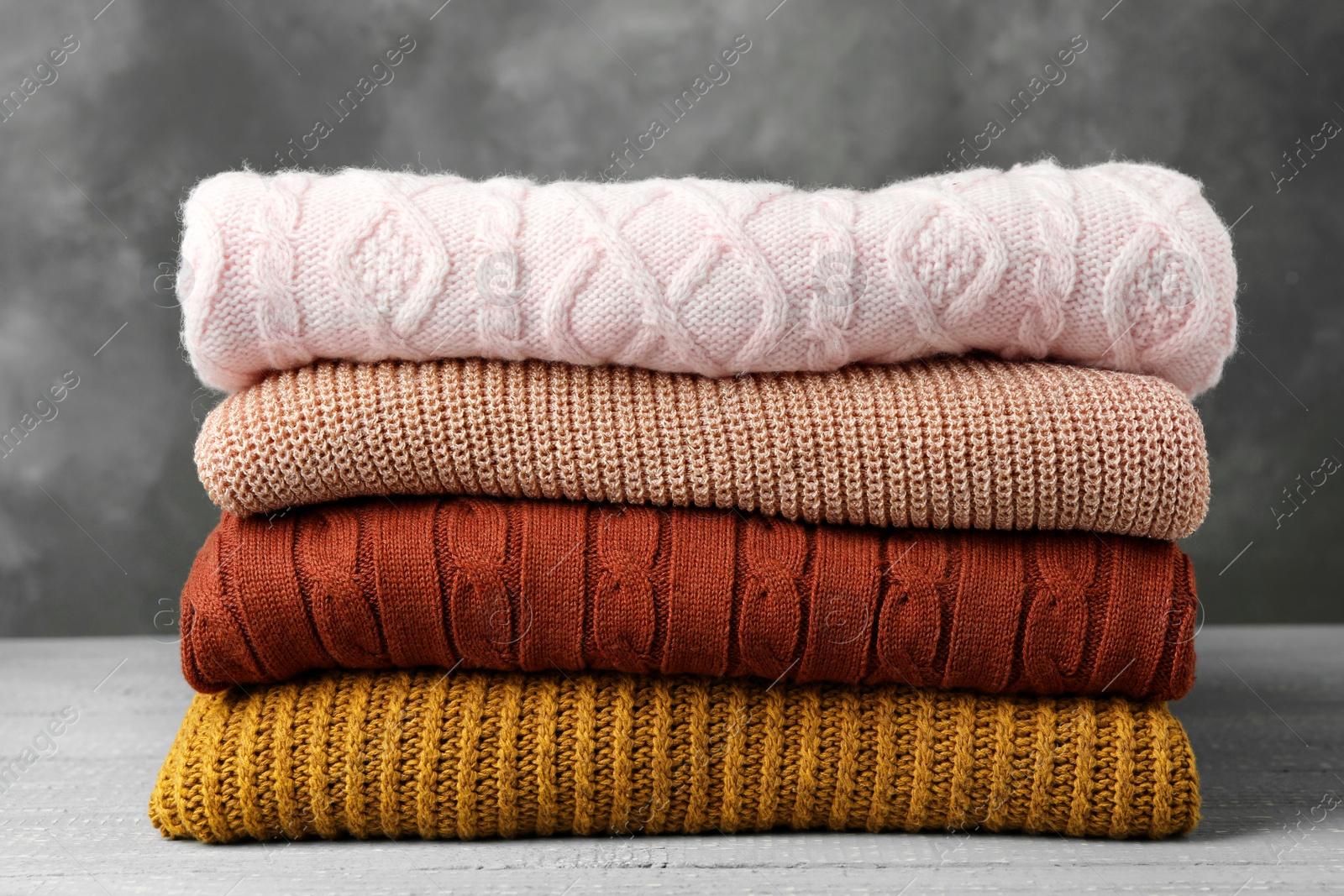 Photo of Stack of warm clothes on wooden table against grey background. Autumn season