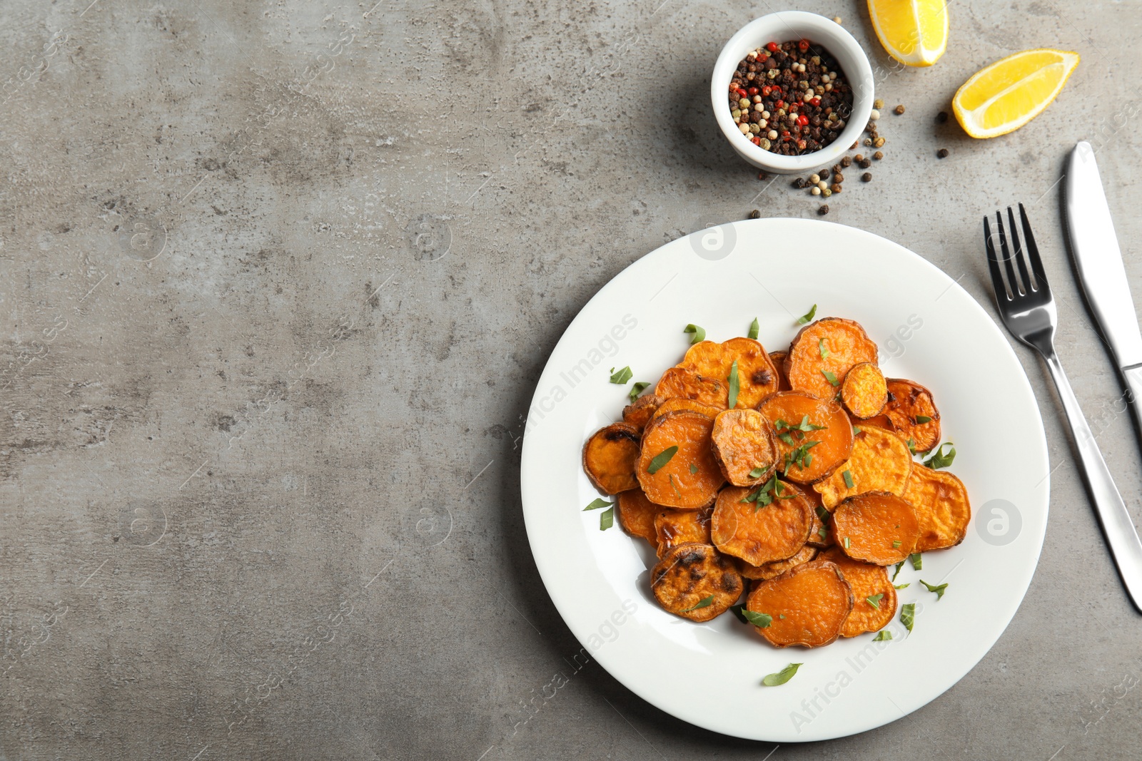 Photo of Plate with baked sweet potato slices served on grey table, top view. Space for text