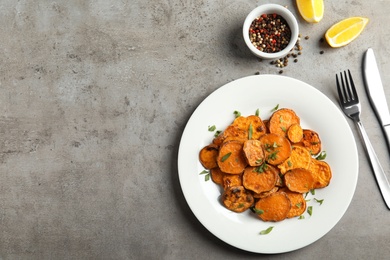 Plate with baked sweet potato slices served on grey table, top view. Space for text