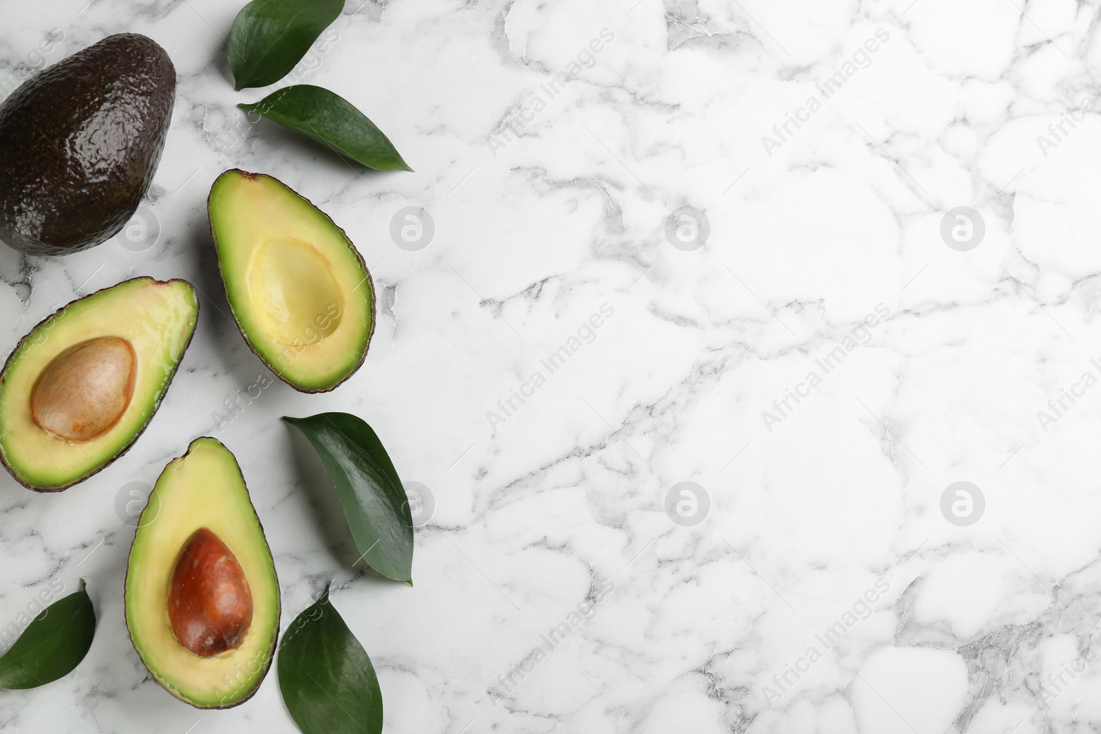 Photo of Whole and cut avocados with green leaves on white marble table, flat lay. Space for text