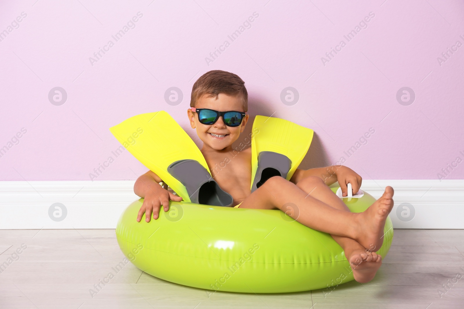 Photo of Cute little boy with inflatable ring and flippers near color wall