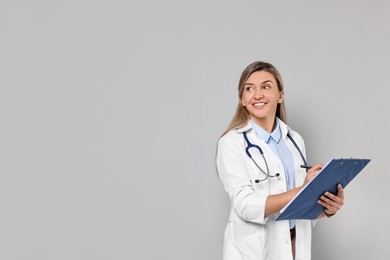 Portrait of happy doctor with stethoscope and clipboard on light grey background, space for text