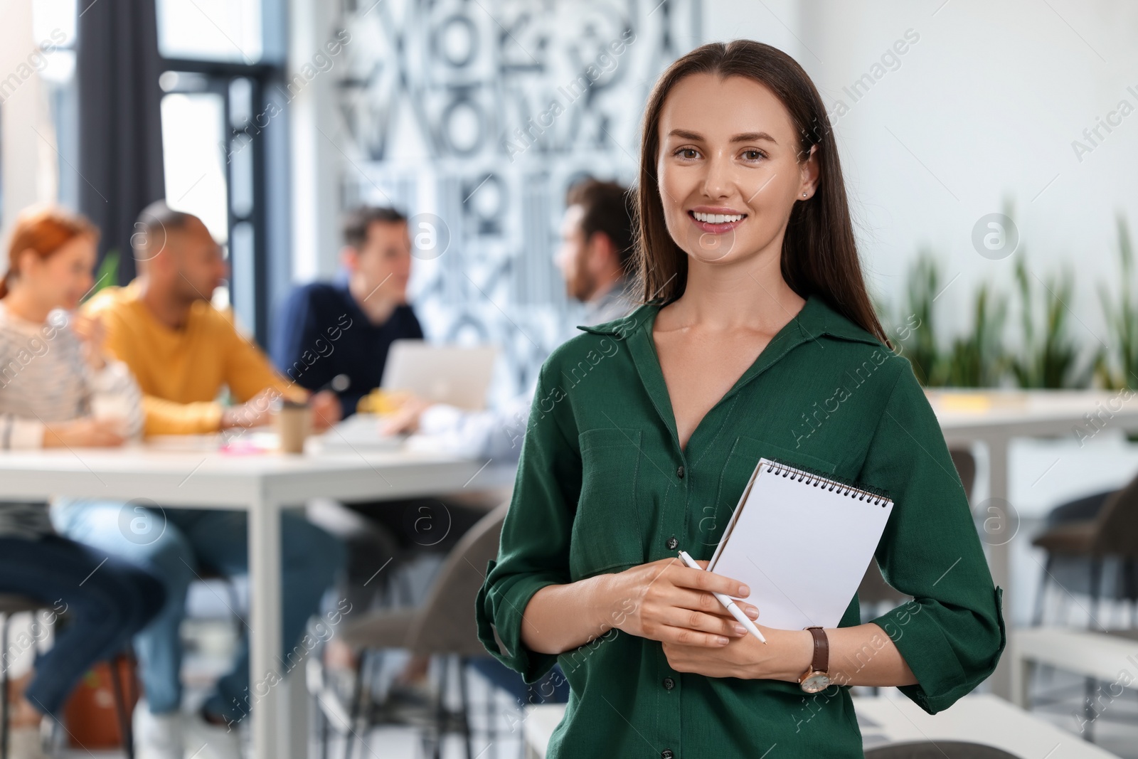 Photo of Team of employees working together in office. Happy woman with notebook and pen indoors, space for text