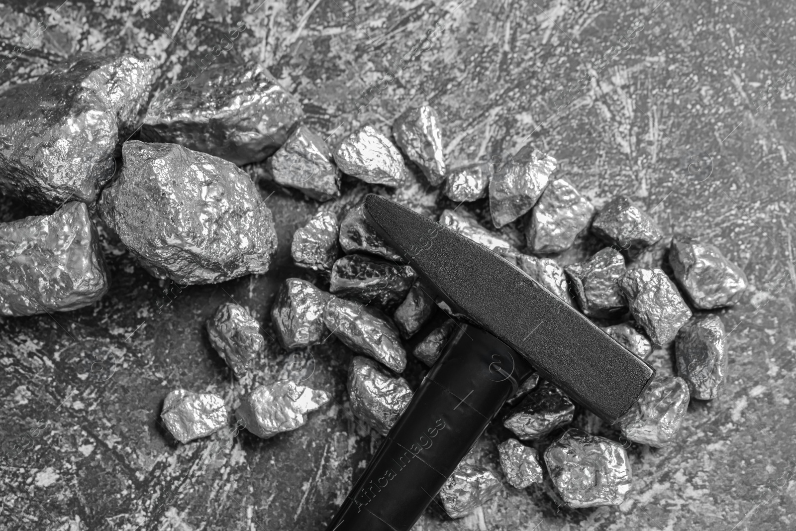 Photo of Pile of silver nuggets and hammer on grey textured table, flat lay