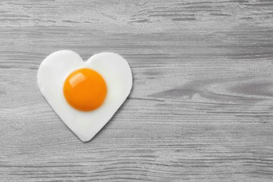 Photo of Heart shaped fried egg on white wooden table, top view