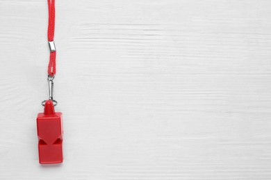 One red whistle with cord on white wooden table, top view. Space for text