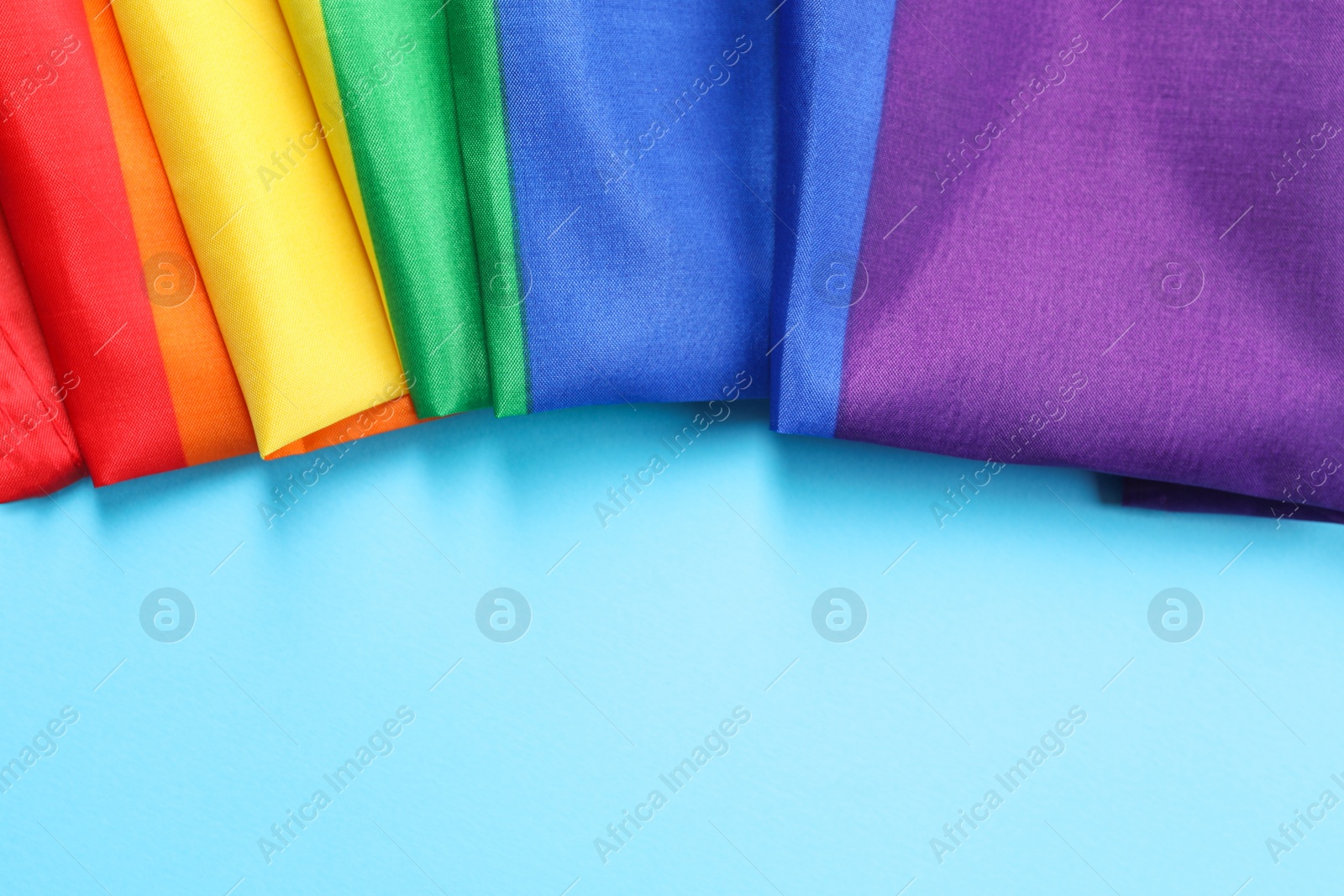 Photo of Rainbow LGBT flag on light blue background, top view. Space for text