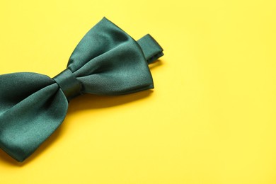 Photo of Stylish green satin bow tie on yellow background, closeup. Space for text