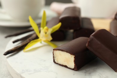 Photo of Glazed curd cheese bars, vanilla pods and flower on board, closeup