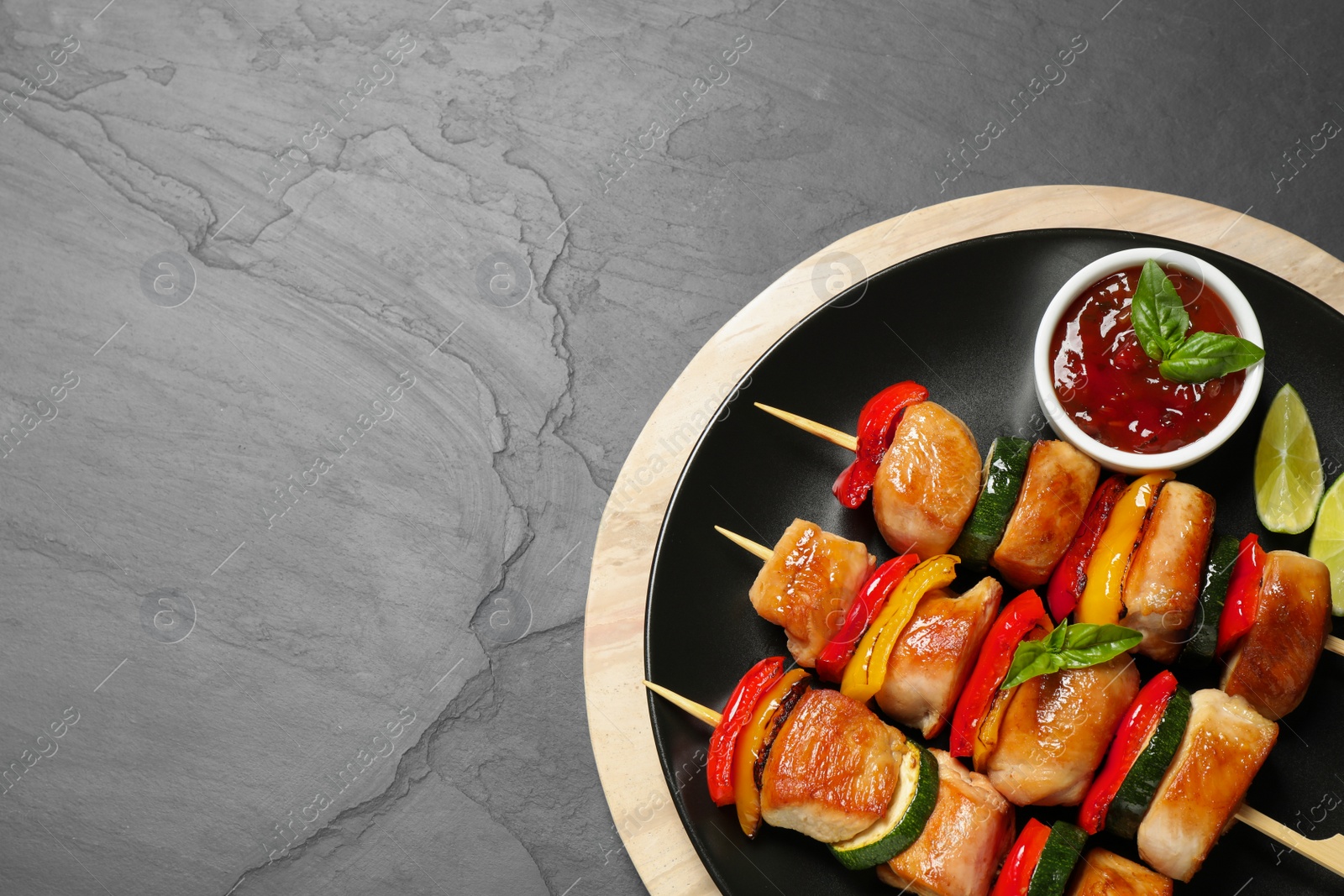 Photo of Delicious chicken shish kebabs with vegetables and sauce on grey table, top view. Space for text