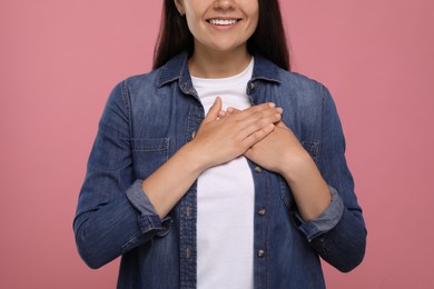Photo of Thank you gesture. Grateful woman holding hands near heart on pink background, closeup