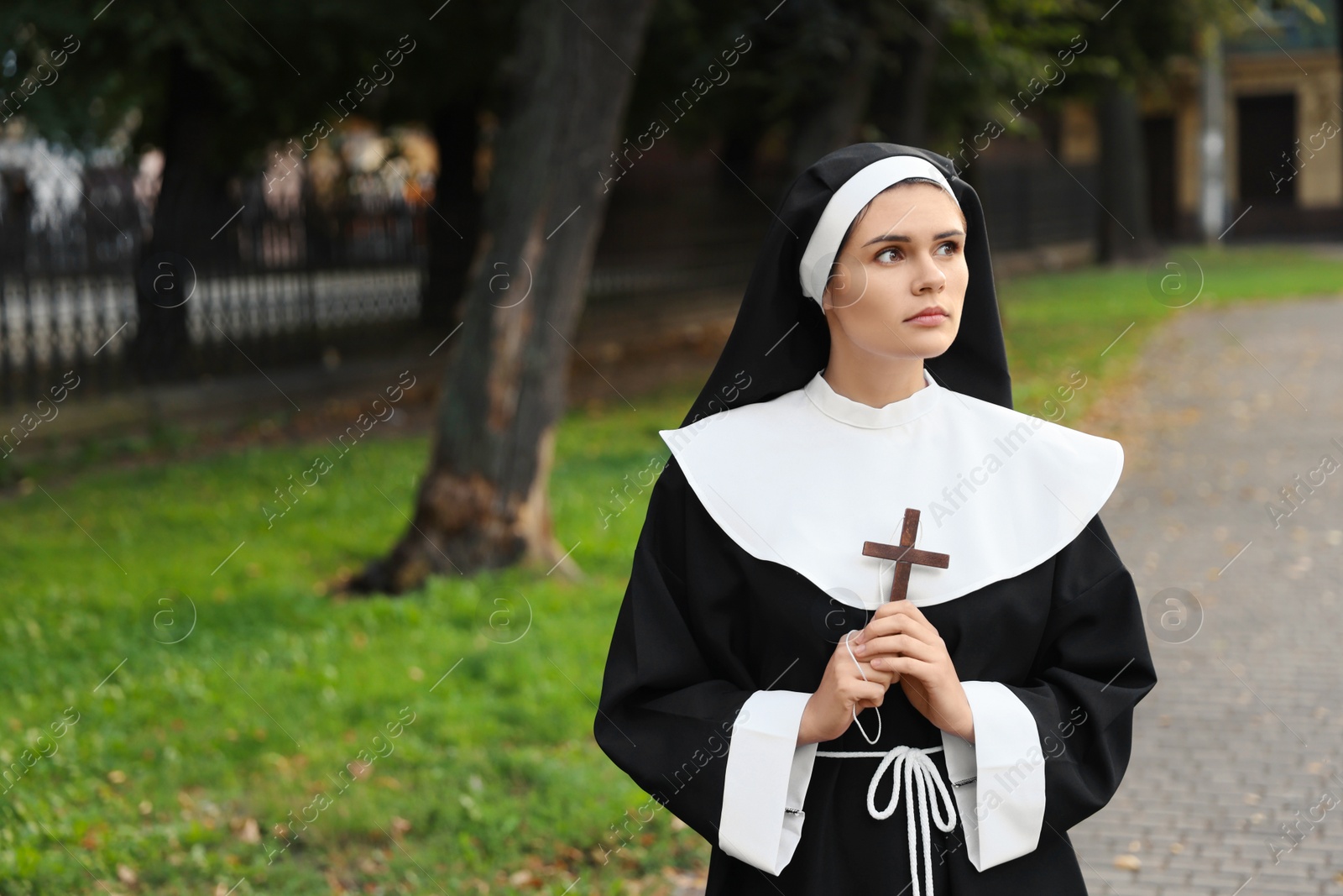 Photo of Young nun with Christian cross in park outdoors, space for text