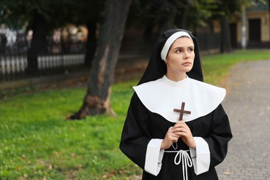 Young nun with Christian cross in park outdoors, space for text