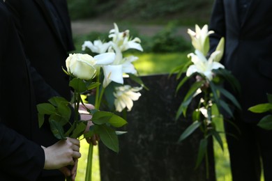 Photo of People with flowers near granite tombstone at cemetery outdoors, closeup and space for text. Funeral ceremony
