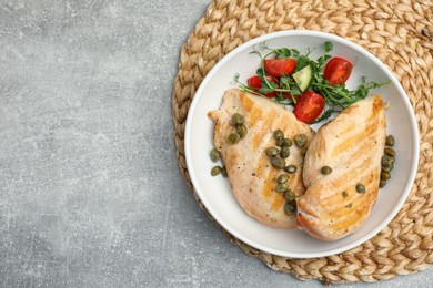 Photo of Delicious cooked chicken fillets with capers and salad on light grey table, top view. Space for text
