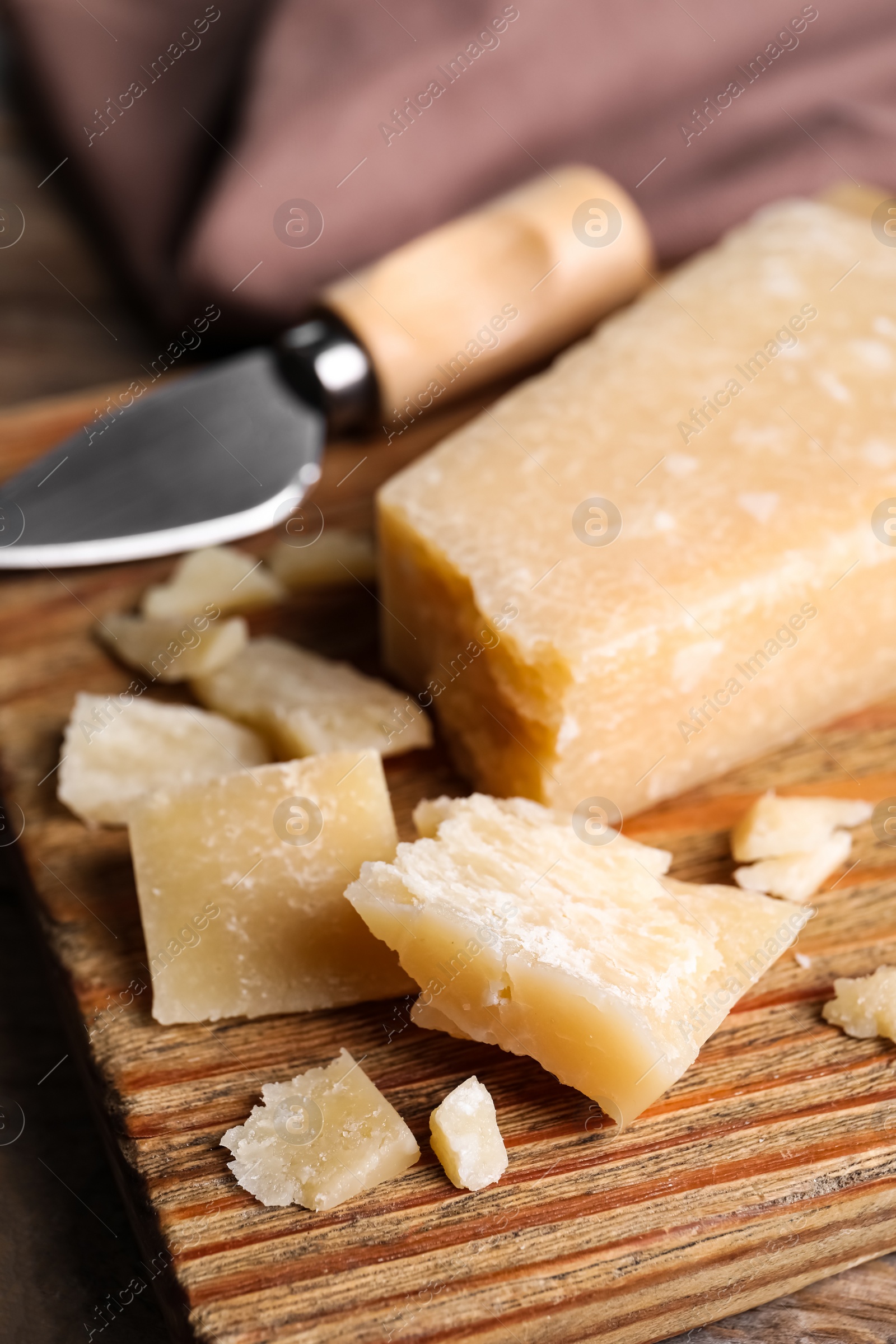 Photo of Parmesan cheese with knife on wooden board, closeup