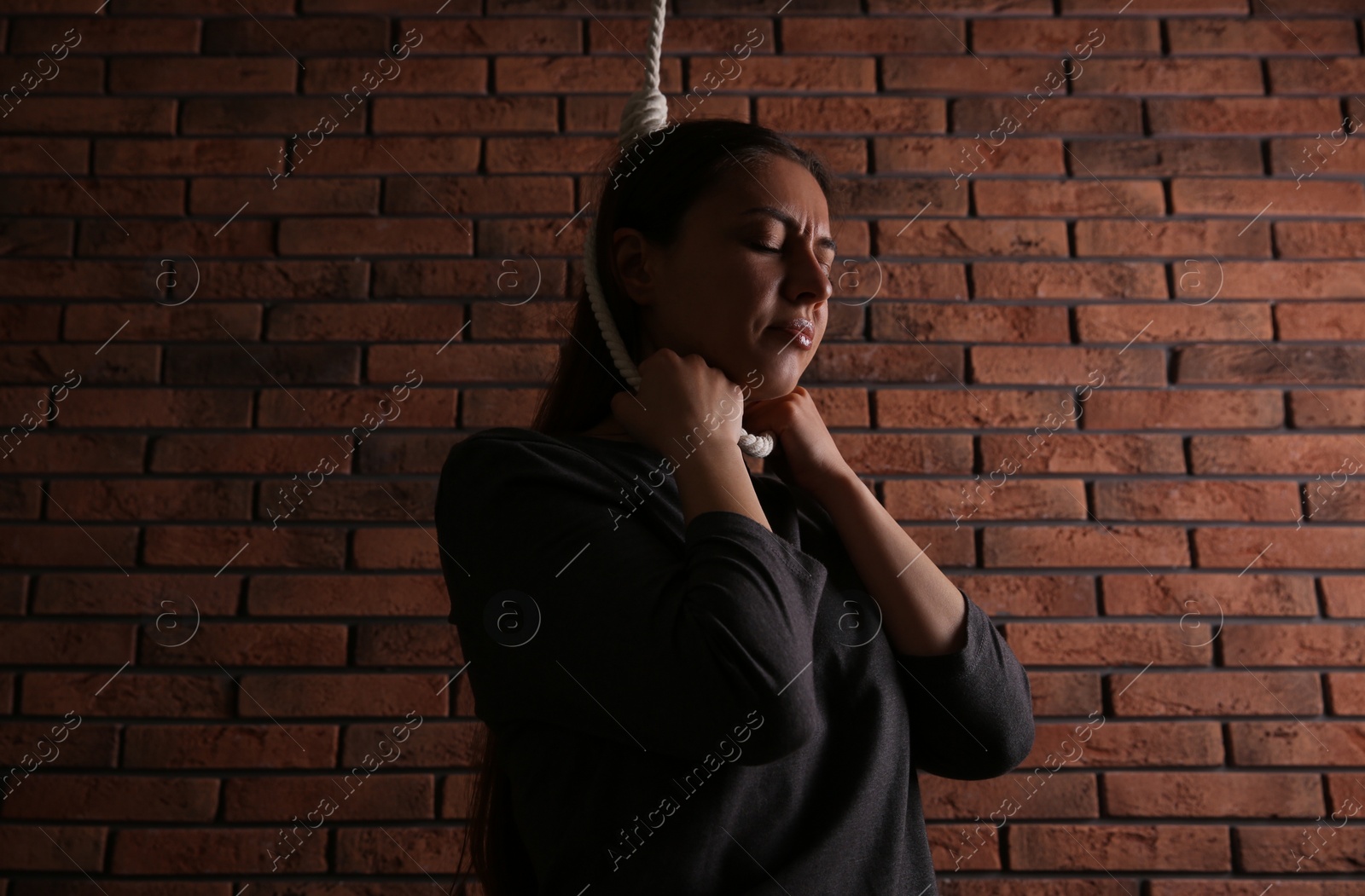 Photo of Depressed woman with rope noose on neck near brick wall