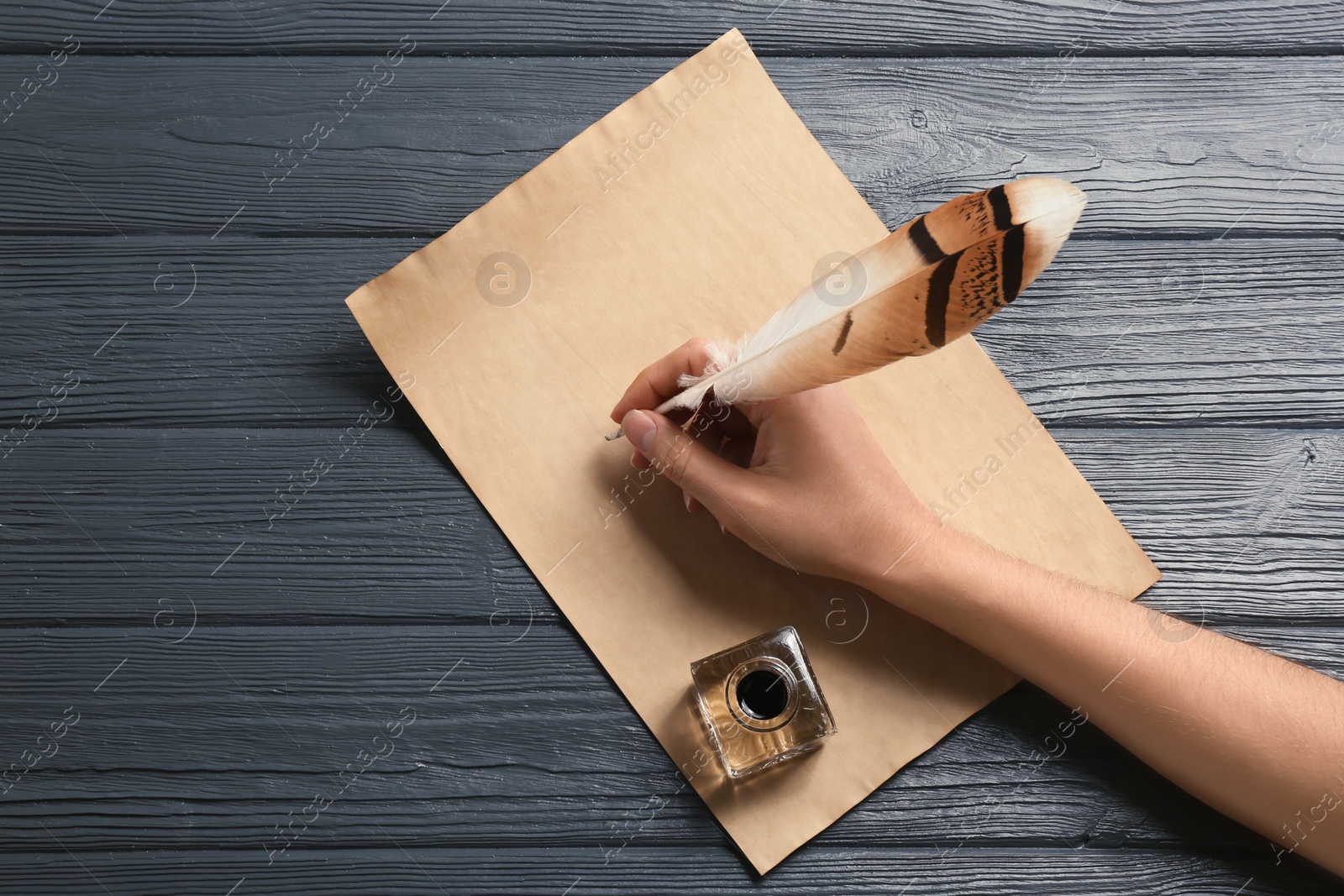 Photo of Woman using feather pen to write with ink on parchment at wooden table, top view. Space for text