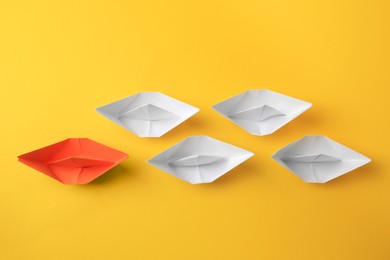 Photo of Group of paper boats following orange one on yellow background, flat lay. Leadership concept