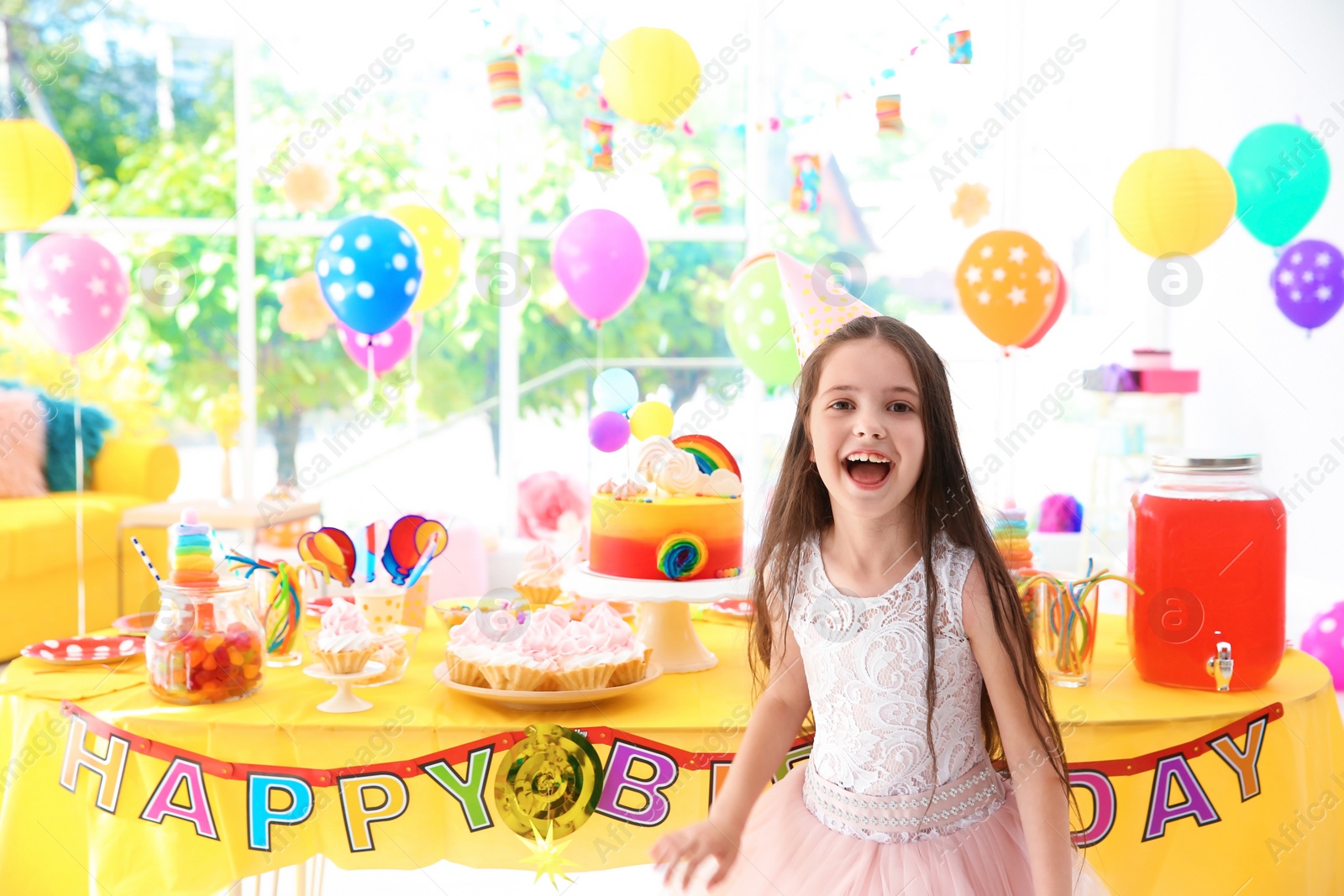 Photo of Cute little girl near table with treats at birthday party indoors