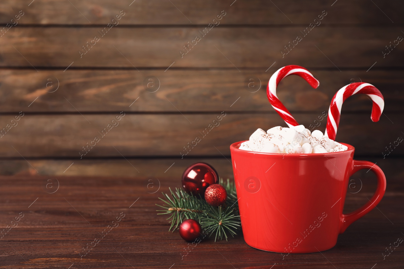 Photo of Red cup of hot drink with marshmallows and candy canes on wooden table. Space for text