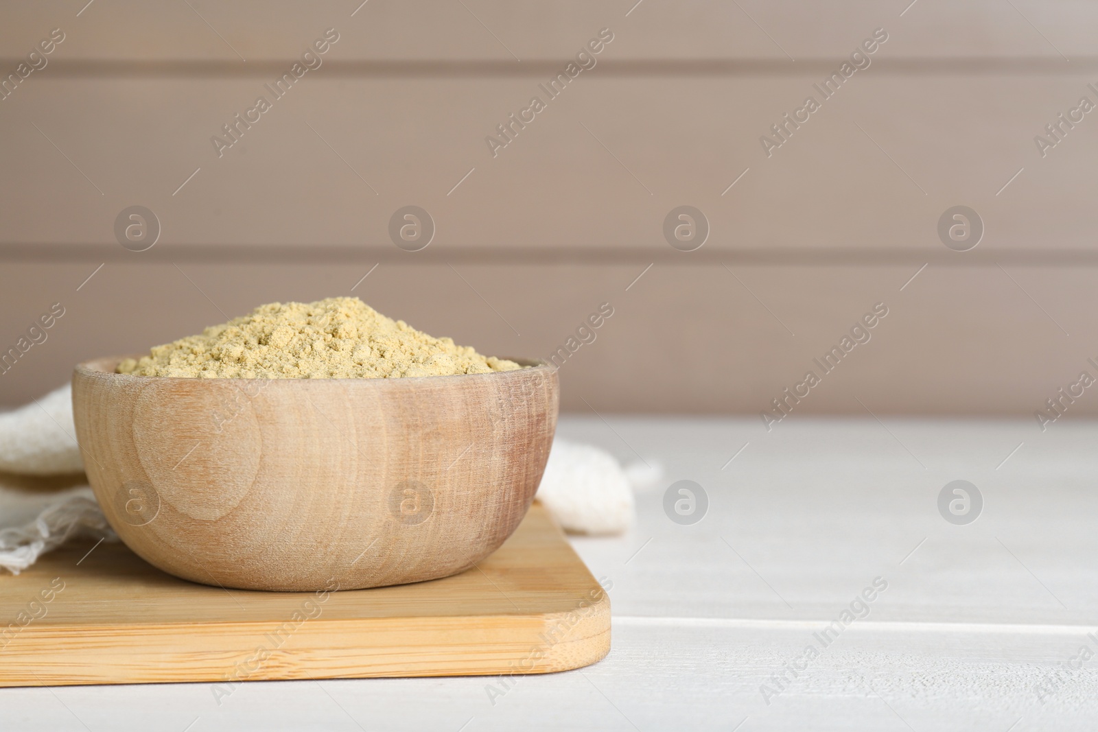 Photo of Bowl of aromatic mustard powder on white wooden table. Space for text