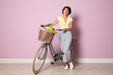 Portrait of beautiful young woman with bicycle near color wall