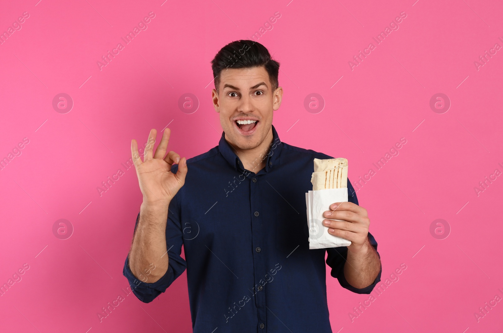 Photo of Emotional man with delicious shawarma on pink background