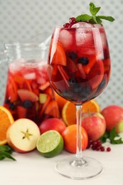 Photo of Glass and jug of Red Sangria with fruits on white wooden table