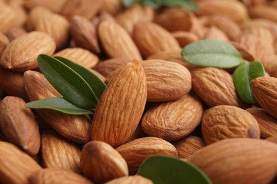Photo of Many delicious almonds and fresh leaves as background, closeup