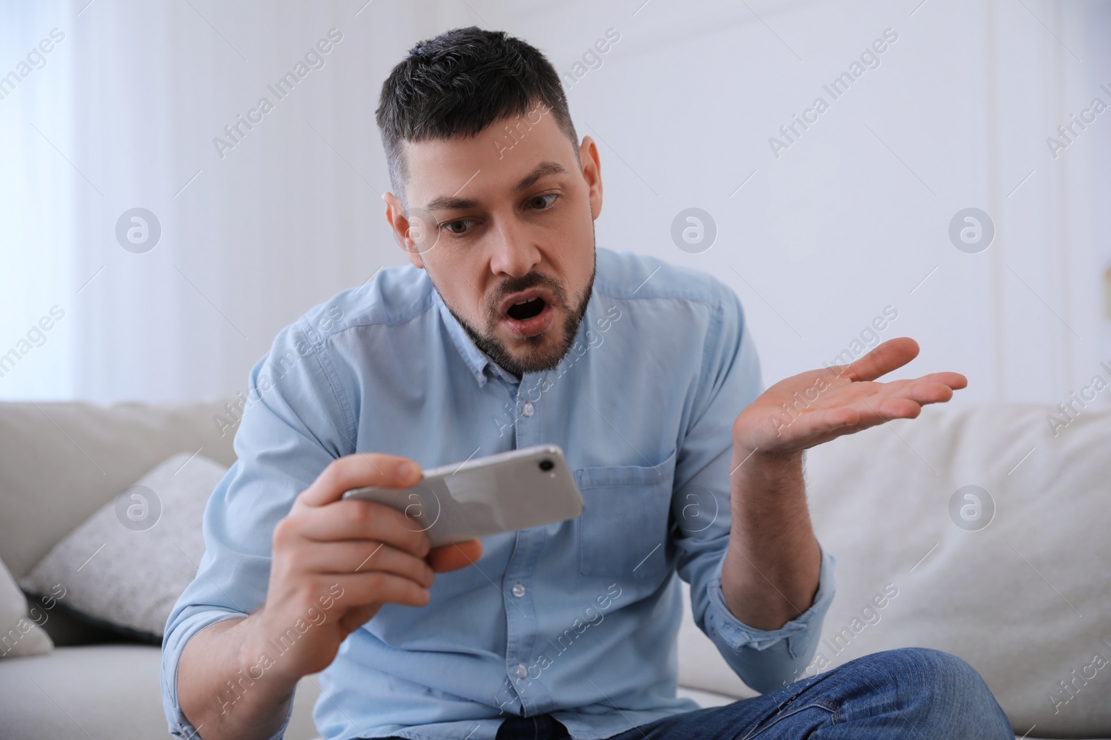 Photo of Emotional man with smartphone at home. Online hate concept