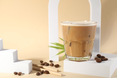 Photo of Refreshing iced coffee with milk in glass and beans on pale yellow background, space for text