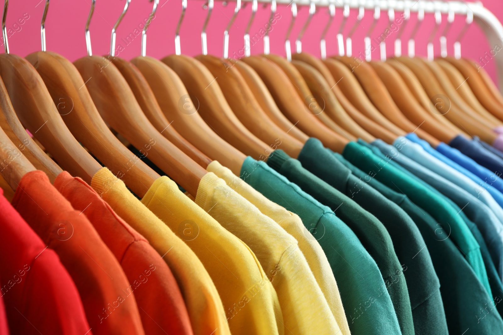 Photo of Rack with bright clothes on pink background. Rainbow colors