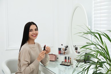 Beautiful woman applying makeup near mirror in room