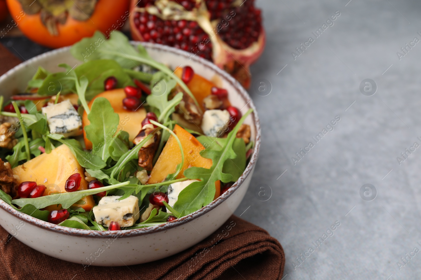 Photo of Tasty salad with persimmon, blue cheese, pomegranate and walnuts served on light grey table, closeup. Space for text